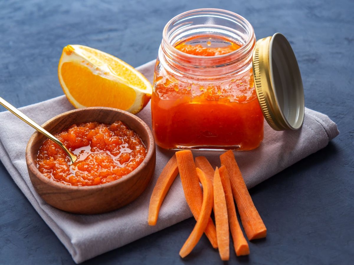 Hasenfrühstück steht auf einem Brett, daneben ein Schälchen mit der Konfitüre. Neben dem geöffneten Glas liegen Karottenstifte und eine Orangenspalte als Deko.