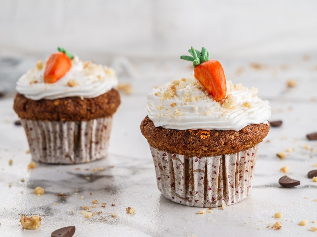 2 Karottenkuchen-Cupcakes, mit Marzipanmöhren dekoriert.