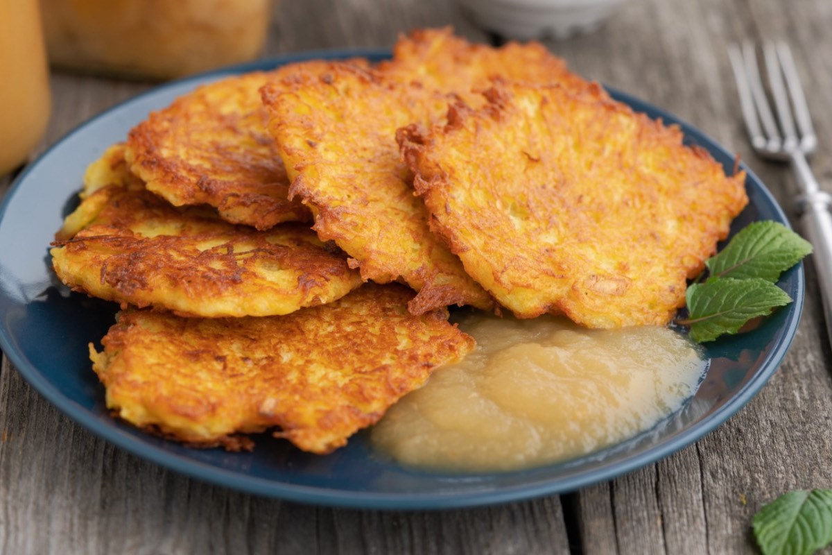 Mehrere Kartoffelpuffer mit Apfelmus auf einem Teller. Daneben liegt eine Gabel.