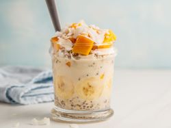 Mango Kokos Overnight Oats im Glas geschichtet und serviert mit einem Strohhalm.