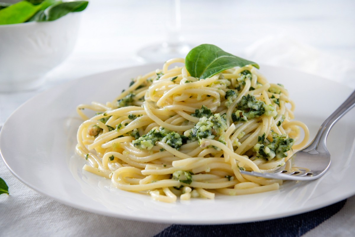 Ein Teller Ofen-Spaghetti mit Spinat und Feta, garniert mit einem Basilikumblatt, auf dem Teller auch eine Gabel.