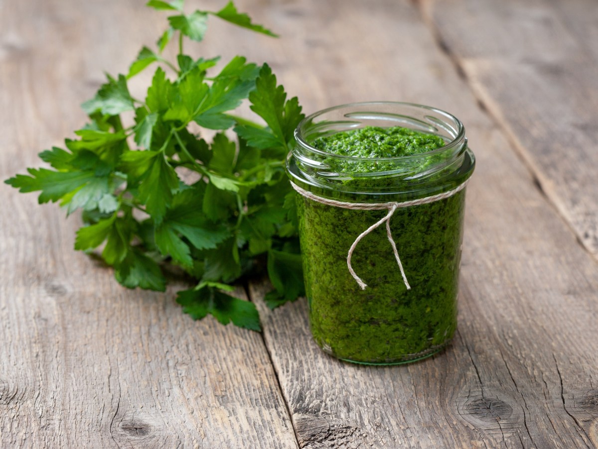 Petersilienpesto in einem Glas auf einer Holzunterlage, daneben ein Bund Petersilie.