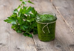 Petersilienpesto in einem Glas auf einer Holzunterlage, daneben ein Bund Petersilie.