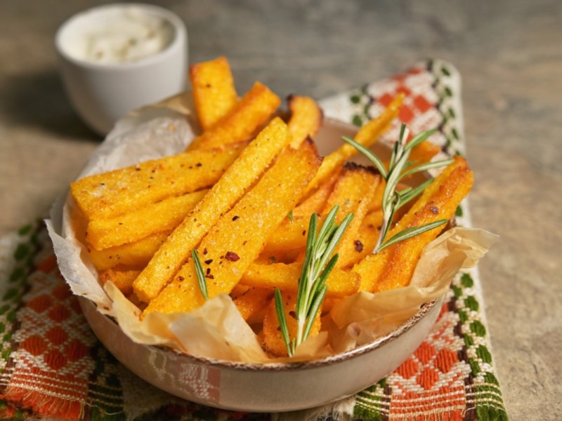 Polenta-Pommes in einer Schüssel. Daneben steht ein Schälchen mit Dip.