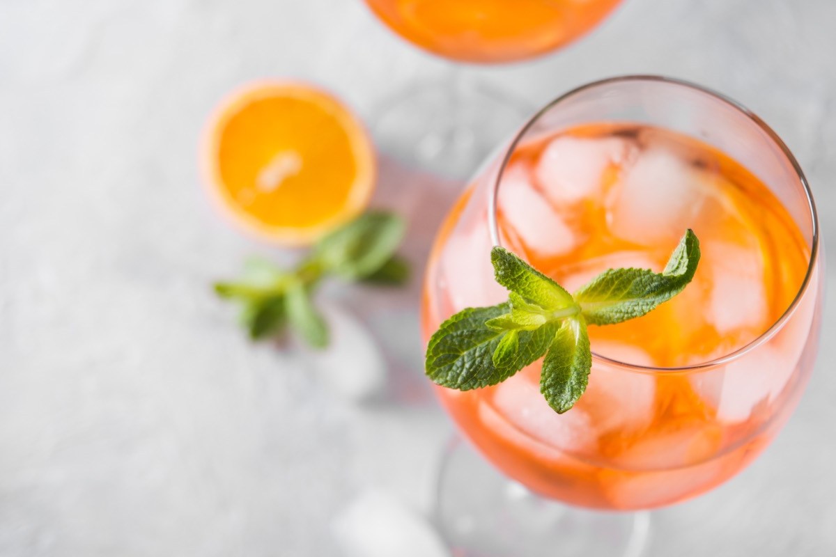 Ein Glas Rhabarber Spritz mit Minze von oben fotografiert. Daneben liegen eine Orangenscheibe und Minzblätter.