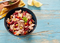 Thunfischsalat in einer blauen Schale auf einem hellblauen Tisch, daneben Zitronen und eine gelbe Serviette.