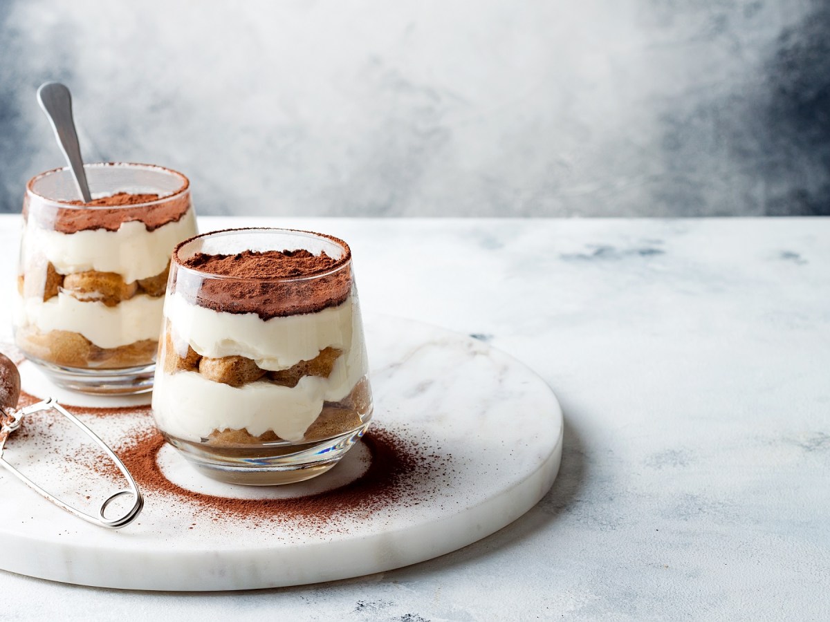 zwei Mal Tiramisu im Glas, die Gläser stehen auf einer runden Marmorplatte.