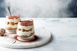 zwei Mal Tiramisu im Glas, die Gläser stehen auf einer runden Marmorplatte.