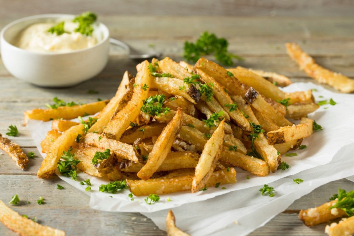 Eine Portion Trüffelpommes mit Petersilie und einer Schale mit Dip.