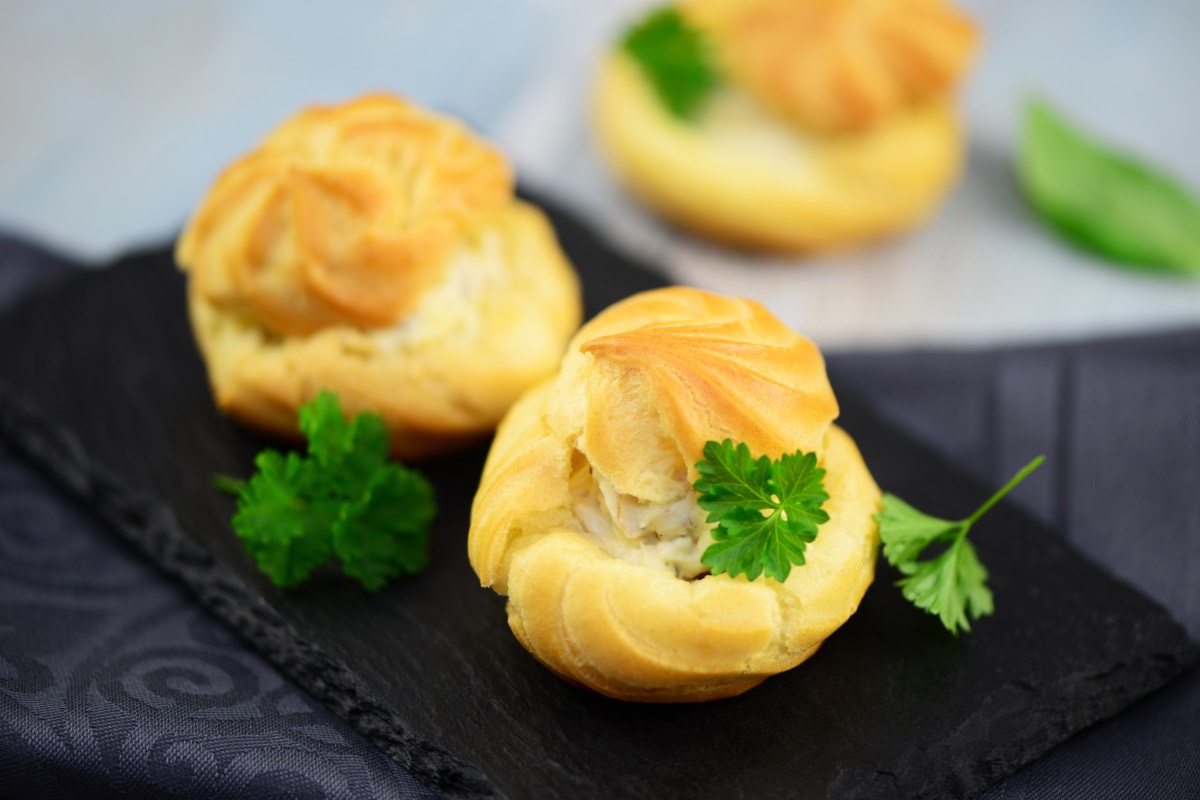 Drei Windbeutel mit Frischkäse-Füllung auf einer Schiefertafel. Garniert sind sie mit Petersilie.