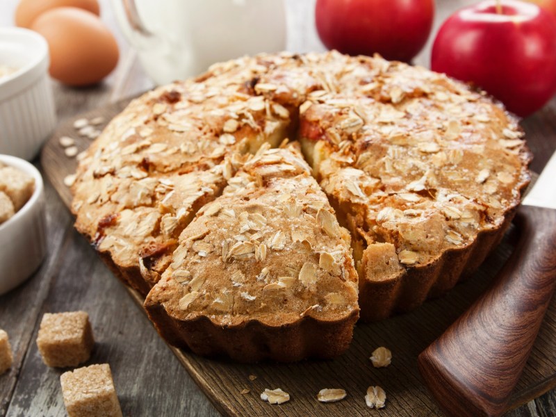 Backform mit Apfel-Haferkuchen auf Tisch mit Äpfeln daneben.