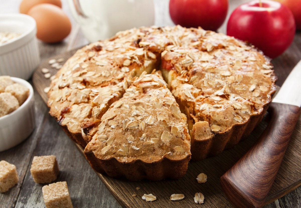 Backform mit Apfel-Haferkuchen auf Tisch mit Äpfeln daneben.