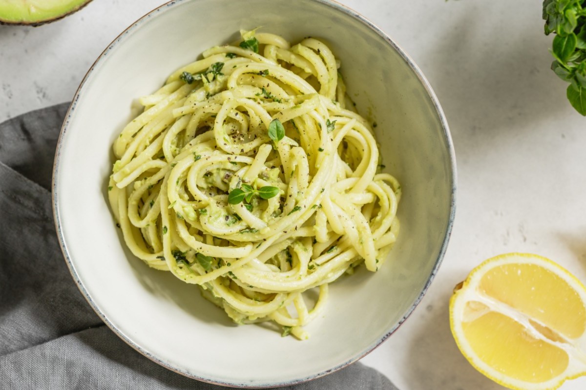 Ein Teller Avocado-Basilikum-Pasta in der Draufsicht. Drumherum liegen frische Zutaten.