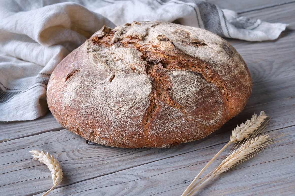 Bauernbrot auf einem Tisch, daneben liegen Weizenähren.