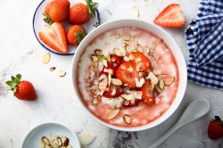 Schüssel mit Erdbeer-Mandel-Porridge und Erdbeeren daneben