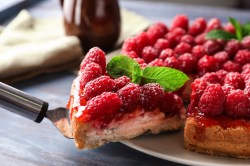 Himbeer-Schmand-Kuchen, aus dem ein Stück mit einem Tortenheber herausgenommen wird.