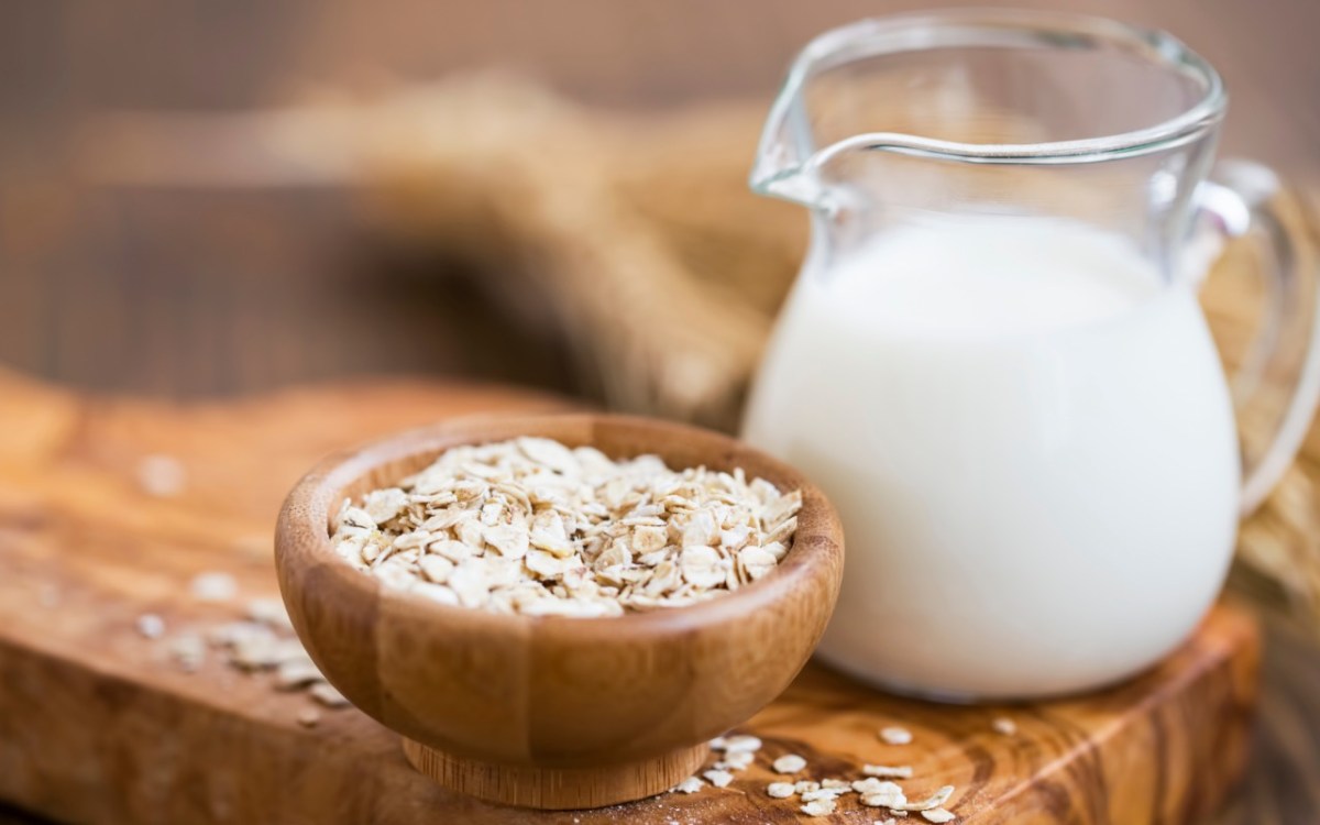 Ist Hafermilch gesund: Eine Glaskaraffe mit Hafermilch- daneben eine Schüssel Haferflocken.