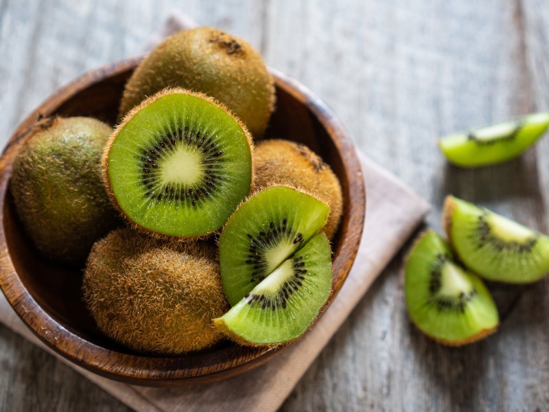 Kiwi mit Schale essen: eine brauen Schüssel mit halbierten Kiwis mit Schale, daneben Kiwiviertel.