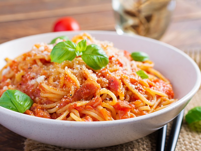 Ein Teller Nudeln mit Tomaten-Frischkäse-Soße mit Parmesan und Basilikum, Nahsicht.