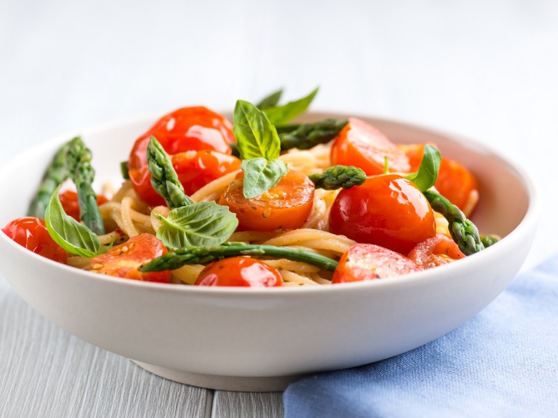 Spargel-Tomaten-Pasta in einer weißen Schüssel, dekoriert mit Basilikum.