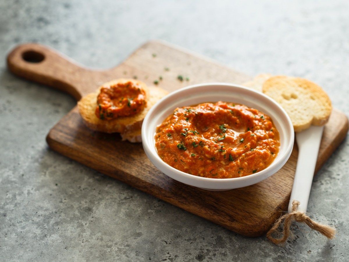 Pesto Calabrese in einer weißen Schale auf einem Holzbrett. Daneben liegt ein Stück Brot.