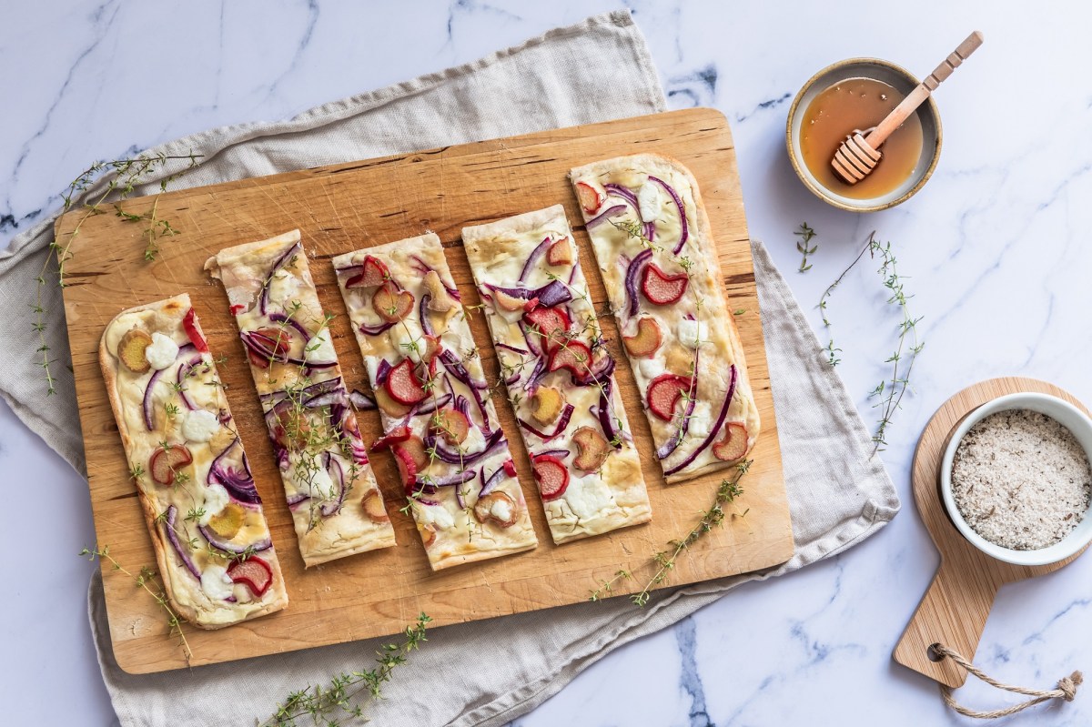 Brett mit Rhabarber-Flammkuchen auf einem hellen Untergrund mit Schale Honig und Salt daneben.