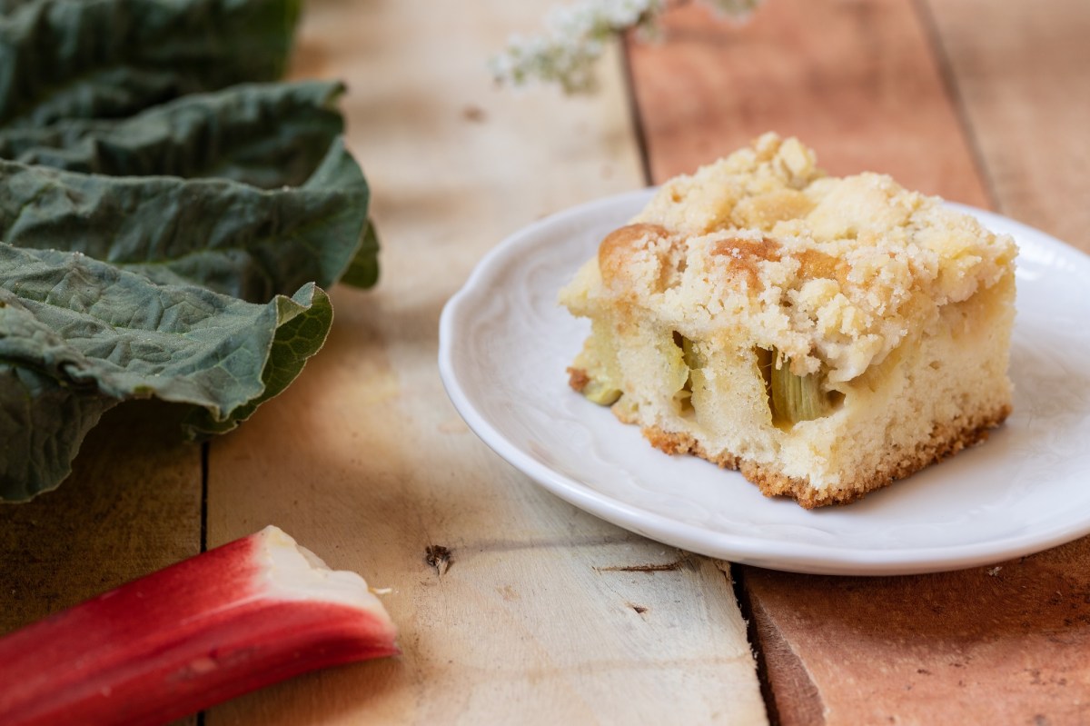 Teller mit Rhabarber-Quark-Streuselkuchen auf Holzuntergrund, daneben Rhabarber