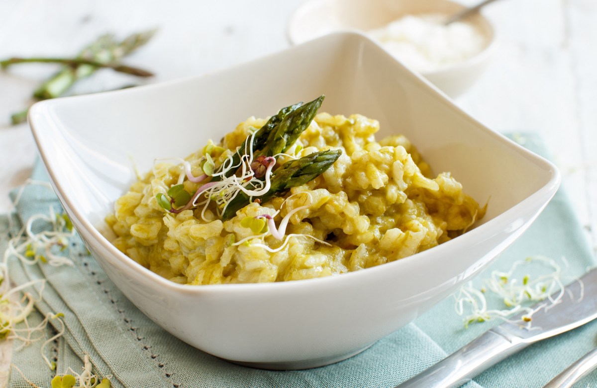 Ein tiefer Teller Risotto mit Sauce hollandaise, grünen Spargelspitzen und Sprossen.