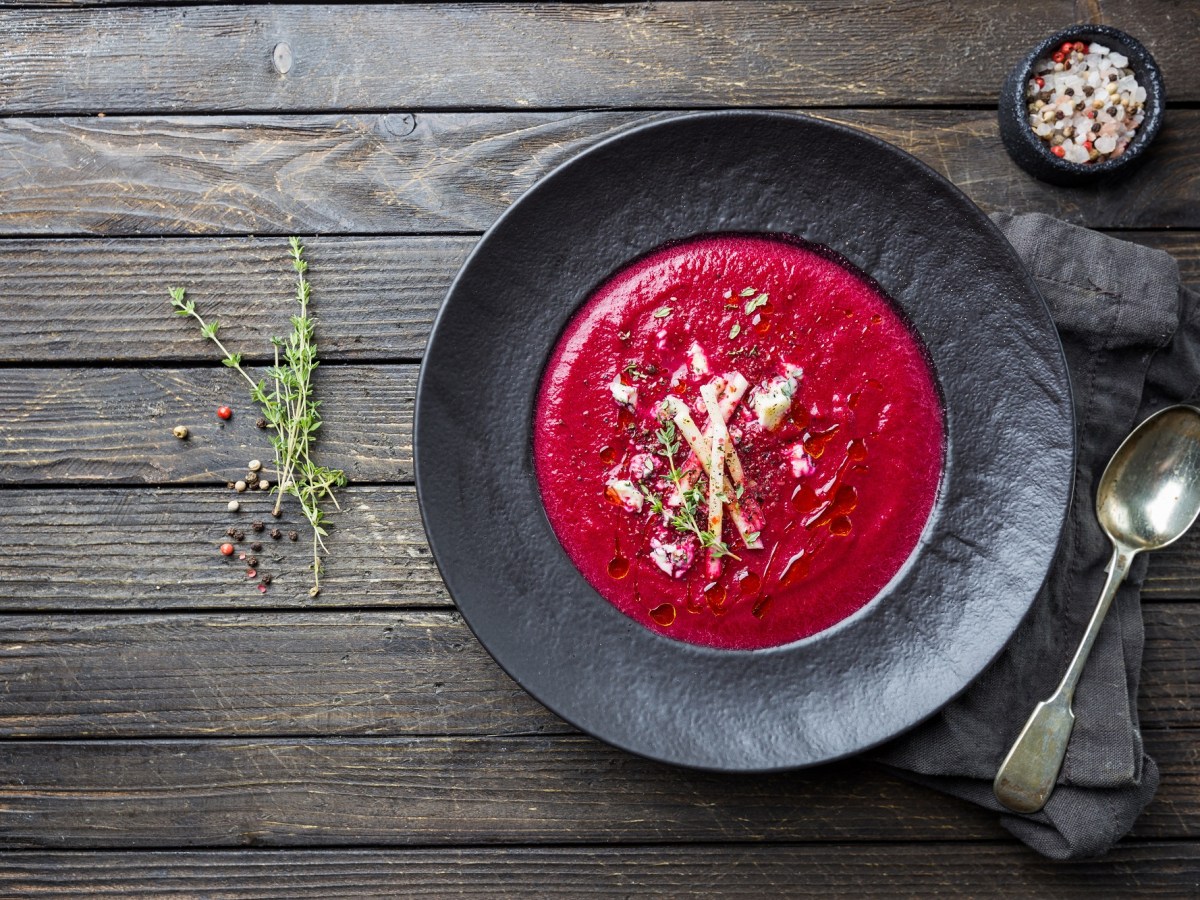 Rote-Bete-Apfel-Suppe, angerichtet auf einem dunkeln Teller auf einem Holztisch.