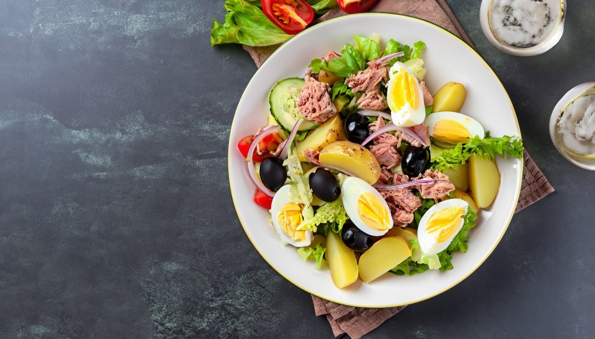 Weißer Teller mit Salade nicoise auf dunklem Untergrund