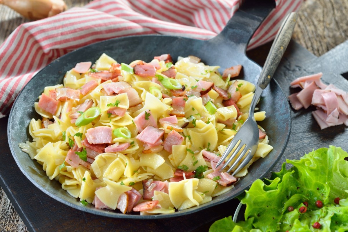 Schinkenfleckerl in einer Pfanne. Daneben ein Salat.