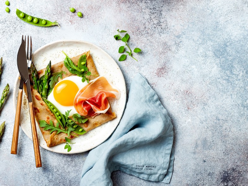 Spargel-Galette auf einem weißen Teller, garniert mit Schinken und grünem Gemüse