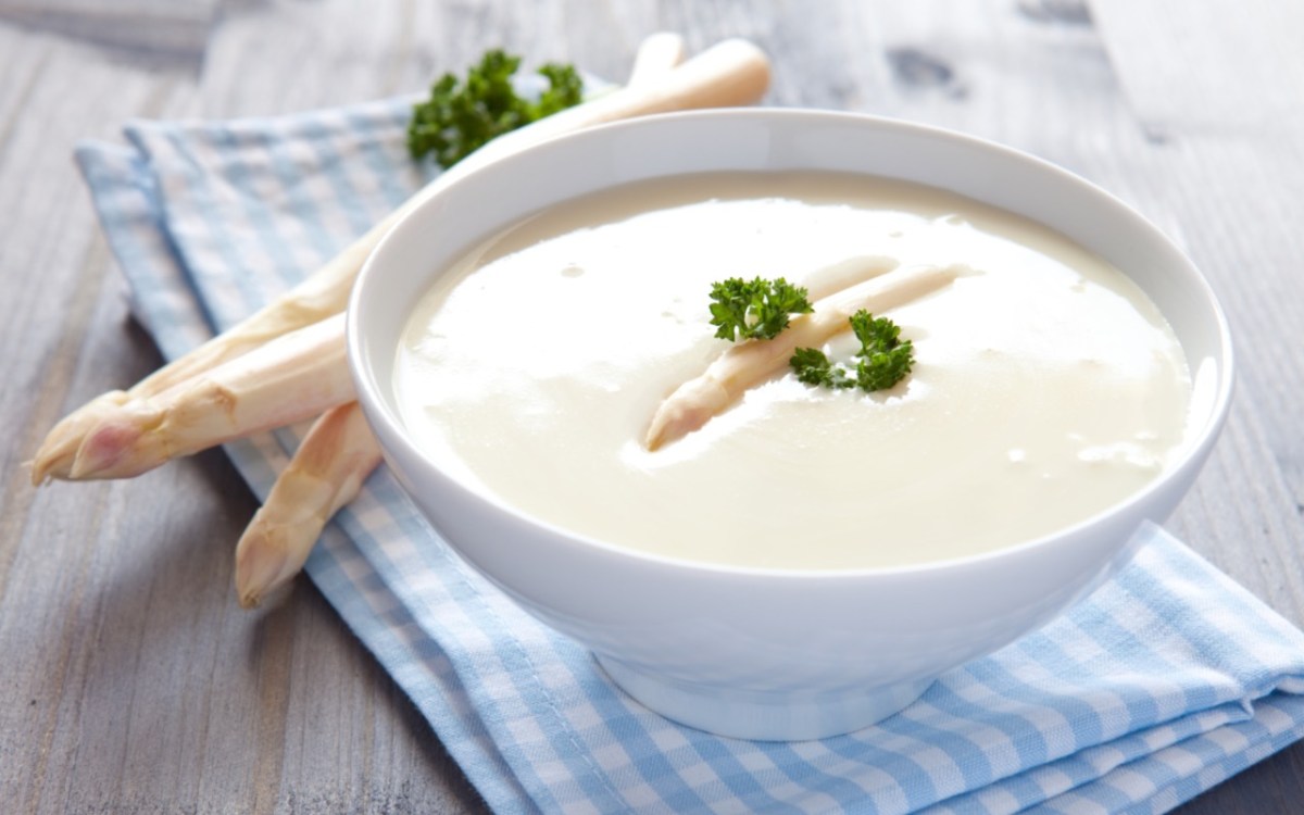 Eine Schüssel Spargelcremesuppe mit Petersilie. Frische Spargelstangen liegen daneben.