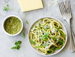 Ein Teller Spaghetti mit Spargelpesto, daneben eine Schale Pesto. Oben am Bildrand liegt ein Stück Parmesan.