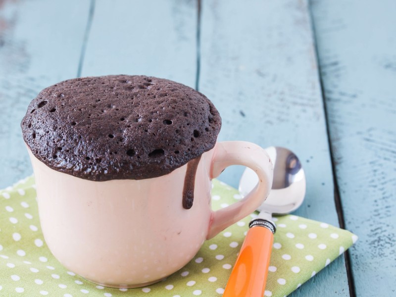 Tassenkuchen aus dem Airfryer, die Tasse steht auf einer grün-weiß gepunkteten Serviette, daneben ein kleiner Löffel.