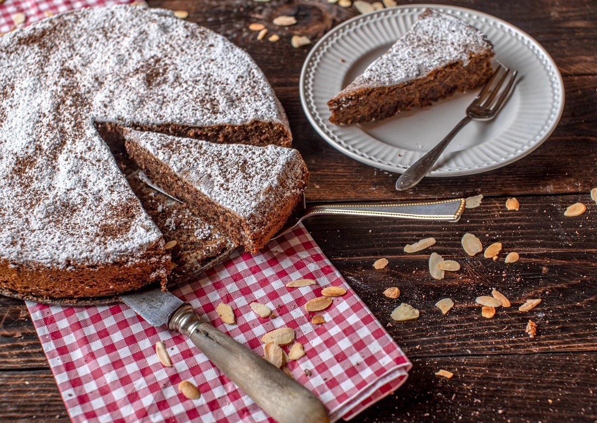 Torta Caprese, italienischer Schoko-Mandel-Kuchen, auf einem weißen Teller. Daneben ein Teller mit einem Stück Kuchen.