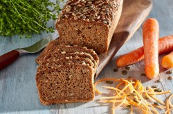 Vollkornbrot mit Möhren, angeschnitten, auf einem Holzbrett. Daneben liegen Möhren.