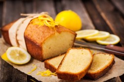 Zitronenkuchen mit fünf Zutaten auf einem Holzbrett. Dabei liegen Zitronenscheiben