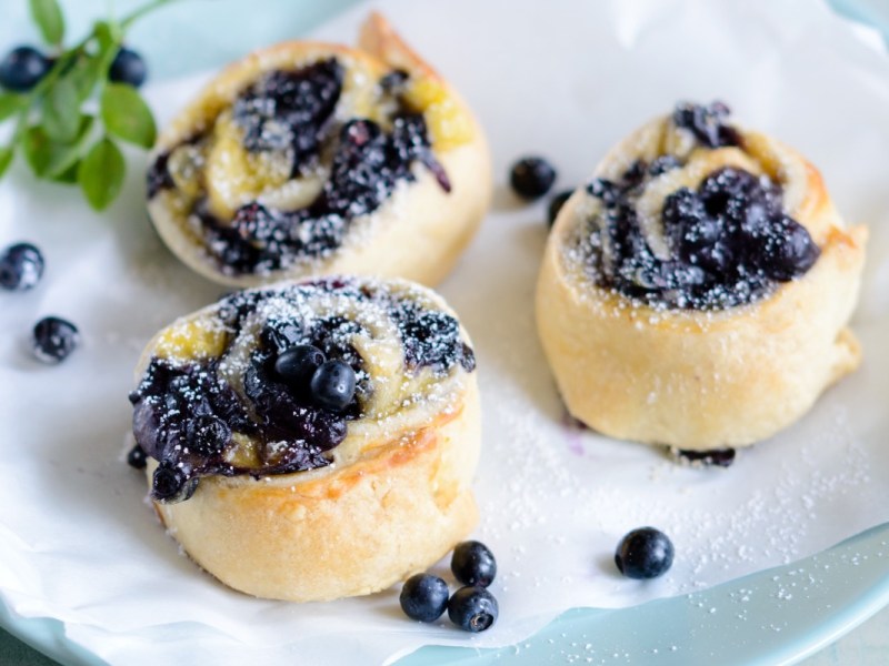 Drei Blaubeer-Hefeschnecken mit Puderzucker auf einem Teller.