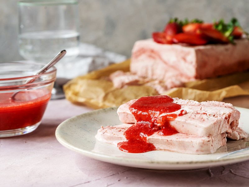 Zwei Scheiben Erdbeer-Parfait mit Fruchtpüree auf einem Teller.