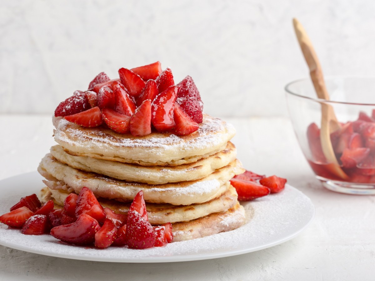 Erdbeer-Pfannkuchen auf einem weißen Teller, bestreut mit Puderzucker.