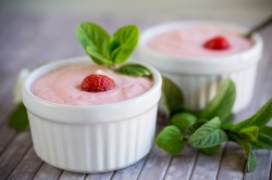 2 Schälchen Erdbeerquark mit einer Erdbeere und Minze garniert.