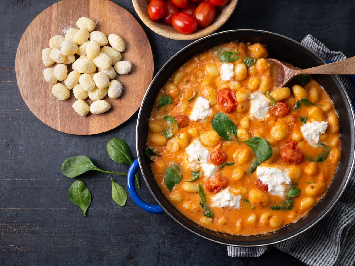 Pfanne mit Gnocchi in Tomatensahnesoße mit Burrata, Brett mit Gnocchi und Tomaten daneben.