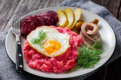 Hamburger Labskaus mit Spiegelei, Rollmops, Roter Bete und Gewürzgurken auf einem Teller, Nahaufnahme.