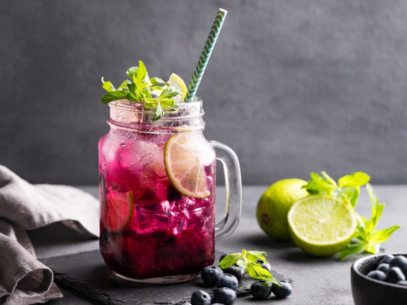 Ein Glas Heidelbeer-Mojito mit frischer Minze und Limetten.