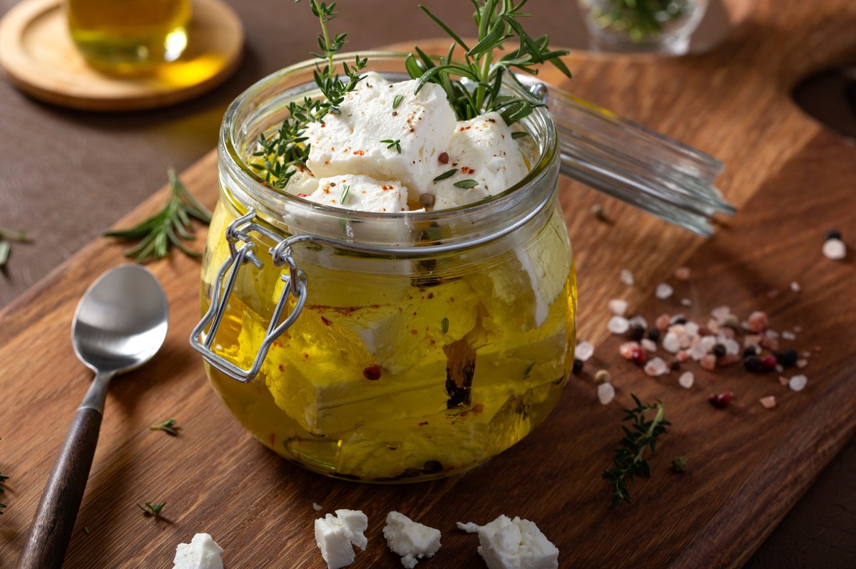 Glas mit mariniertem Feta auf einem Holzbrett