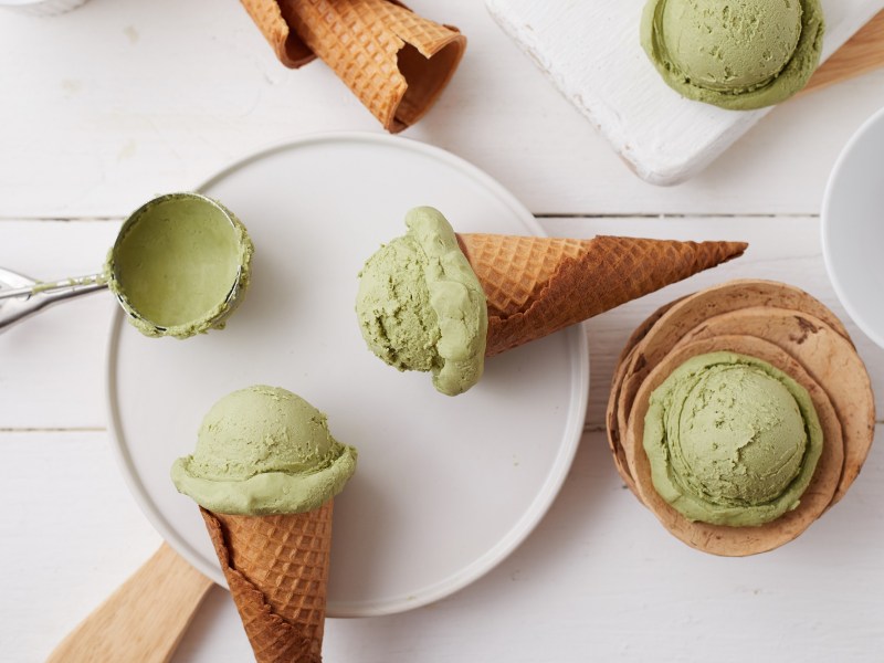 Einige Kugeln Matcha-Eis, einige in Waffeln, liegen auf einem weißen Teller.