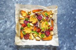 Ofengemüse mit Halloumi auf einem Blech. Dieses steht auf einem blauen Hintergrund.