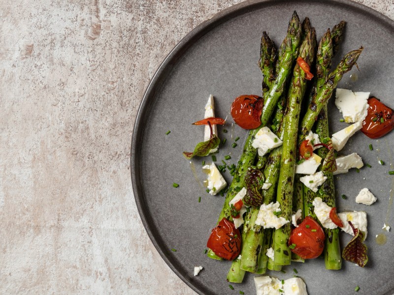 Ofenspargel mit Tomaten und Feta auf einem Teller, Draufsicht.