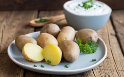 Pellkartoffeln auf einem Teller. Einige sind halbiert. Im Hintergrund steht eine Schüssel mit Kräuterquark.